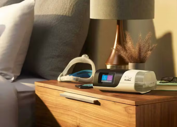 Autocpap Airsense 11 e máscara Resmed sobre uma mesa de cabeceira em um ambiente que transmite tranquilidade no meio da tarde.